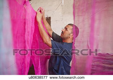 Stock Photo - Man hanging up dyed fabric in traditional milliners workshop. Fotosearch