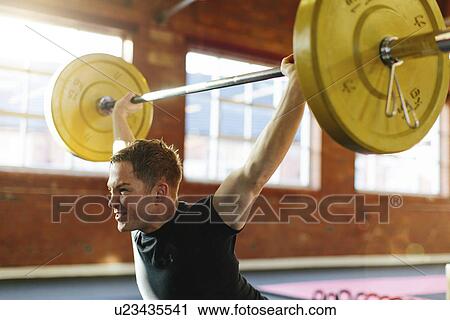 Stock Image - Man lifting weights in gymnasium. Fotosearch