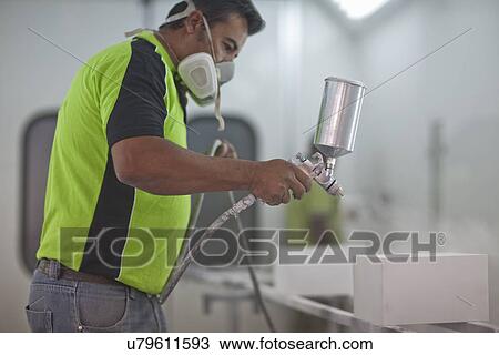 Stock Image - Man spraying wooden products in carpenters workshop. Fotosearch