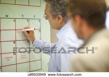 Stock Photo - Mature businessman organizing timetables in office. Fotosearch