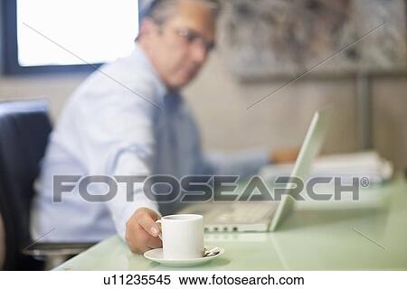 Mature businessman taking a coffee break in office View Large Photo Image Stock Photography - Mature businessman taking a coffee break in office. Fotosearch