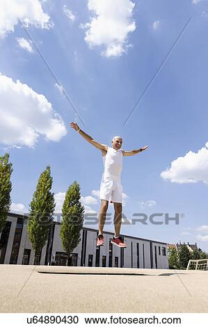 Stock Image - Mature man doing jump exercise in park. Fotosearch