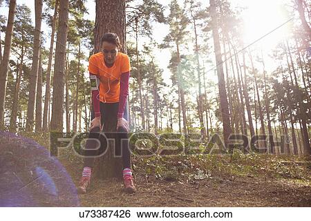 Stock Photograph - Mature woman runner taking a break in a forest. Fotosearch