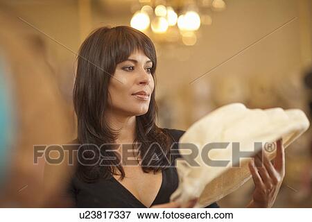 Stock Photo - Mid adult woman looking at hat in milliners shop. Fotosearch