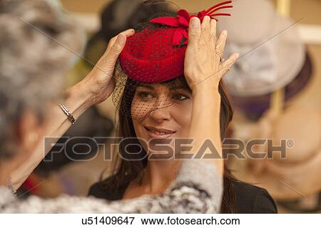 Stock Photo - Milliner adjusting hat for customer in shop. Fotosearch