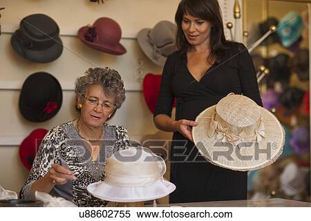 Stock Photography - Milliner adjusting hat for customer in shop. Fotosearch