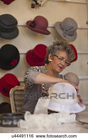 Milliner attaching decoration to hat in shop View Large Photo Image Stock Photograph - Milliner attaching decoration to hat in shop. Fotosearch