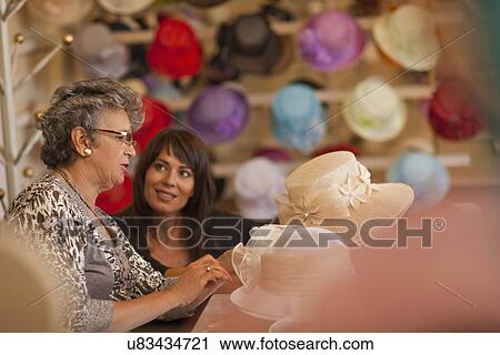 Stock Image - Milliner decorating hat for customer in shop. Fotosearch