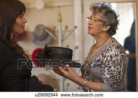 Picture - Milliner showing hat to customer in shop. Fotosearch