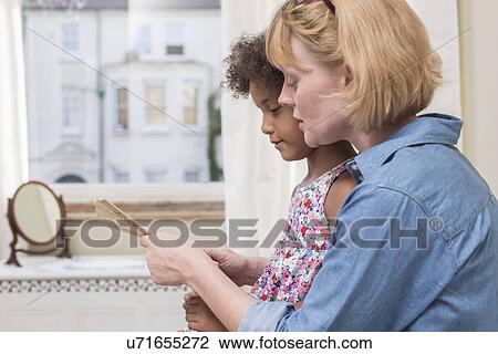 Stock Image - Mother and daughter looking at hand-held fan. Fotosearch