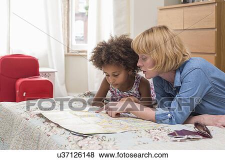 Stock Photo - Mother and daughter lying on bed, looking at map. Fotosearch