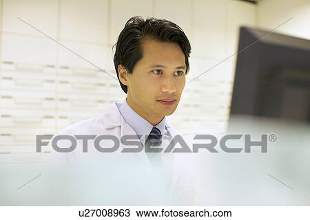 Stock Image - Pharmacist working on computer in pharmacy. Fotosearch