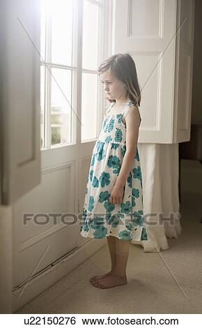 Stock Photograph - Portrait of a girl standing looking out of bedroom window. Fotosearch