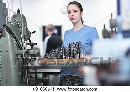 Stock Image - Portrait of female engineer holding a tray of drillbits. Fotosearch