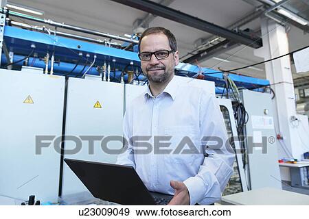 Portrait of manager holding laptop in workshop View Large Photo Image Stock Photo - Portrait of manager holding laptop in workshop. Fotosearch