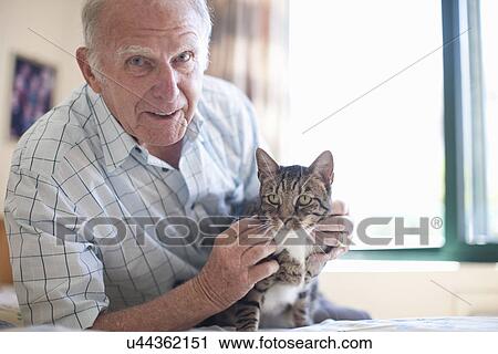 Stock Image - Portrait of senior man petting domestic cat. Fotosearch