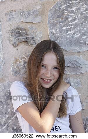 Stock Image - Portrait of shy smiling girl leaning against wall. Fotosearch