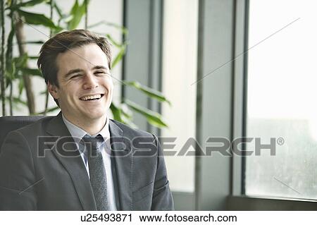 Stock Image - Portrait of young businessman at office desk. Fotosearch