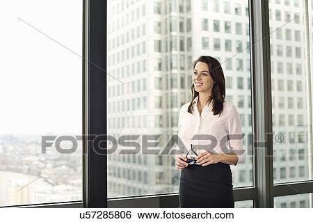 Stock Photograph - Portrait of young businesswoman looking out of office window. Fotosearch
