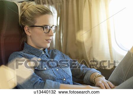 Stock Image - Portrait of young woman sitting on train. Fotosearch