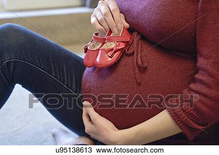 Pregnant woman holding baby shoes to her bump View Large Photo Image Stock Image - Pregnant woman holding baby shoes to her bump. Fotosearch