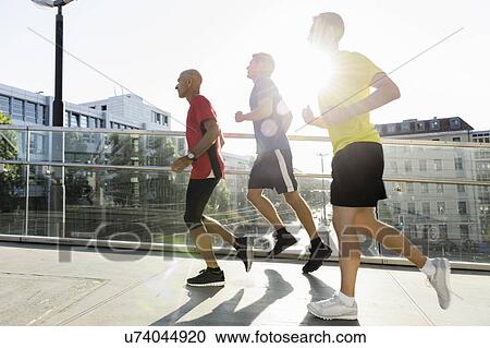 Stock Image - Runners crossing bridge, Munich, Germany. Fotosearch