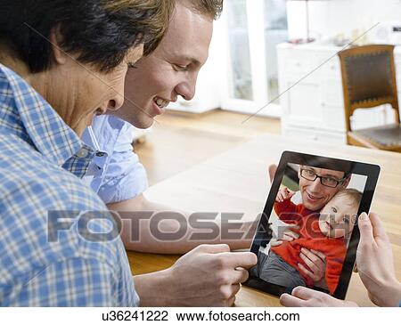 Senior woman and young man looking at image of father and baby son on digital tablet View Large Photo Image Stock Image - Senior woman and young man looking at image of father and baby son on digital tablet. Fotosearch
