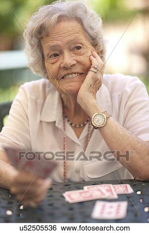 Stock Photograph - Senior woman playing cards at garden table. Fotosearch