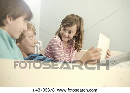 Sister and older brothers on sofa using digital tablet View Large Photo Image Stock Photo - Sister and older brothers on sofa using digital tablet. Fotosearch