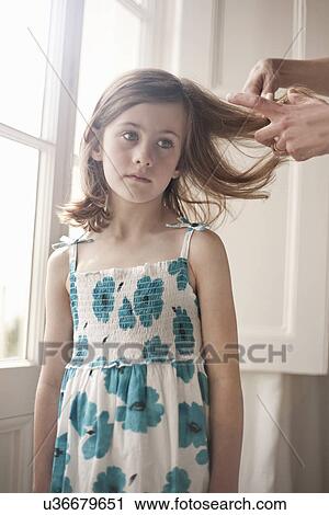 Stock Image - Sulky girl having her hair brushed by her mother. Fotosearch