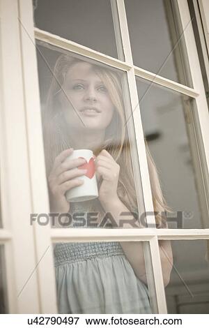 Stock Photo - Teenage girl holding a coffee mug looking out of window. Fotosearch