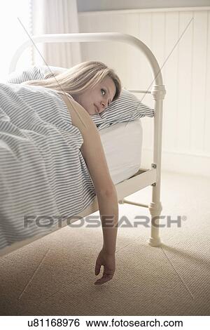 Stock Photograph - Teenage girl lying in bed with arm dangling. Fotosearch