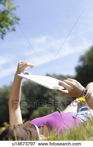 Teenage girl lying in park looking at digital tablet View Large Photo Image Stock Photo - Teenage girl lying in park looking at digital tablet. Fotosearch
