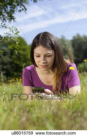Teenage girl lying in park looking at cellphone View Large Photo Image Stock Photo - Teenage girl lying in park looking at cellphone. Fotosearch