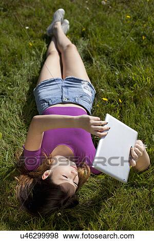 Teenage girl relaxing in park looking at digital tablet View Large Photo Image Stock Photo - Teenage girl relaxing in park looking at digital tablet. Fotosearch