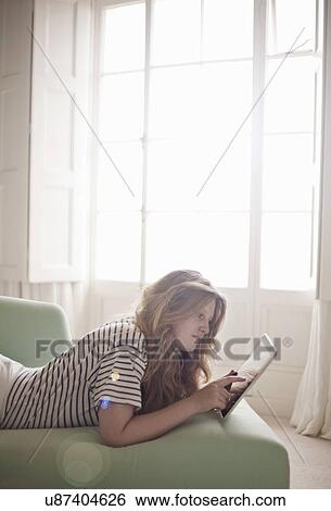 Teenage girl relaxing on chaise longue using digital tablet View Large Photo Image Stock Photograph - Teenage girl relaxing on chaise longue using digital tablet. Fotosearch