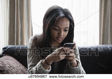 Stock Photo - Teenage girl sitting on sofa texting on smartphone. Fotosearch