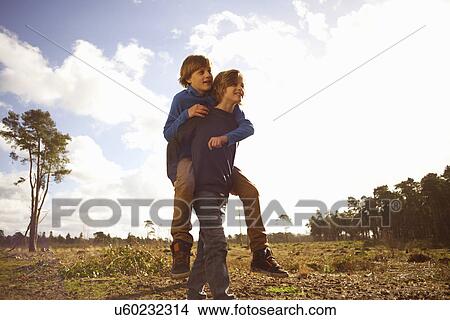 Picture - Twin brothers playing piggy back in forest clearing. Fotosearch