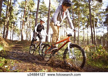 Stock Photo - Twin brothers racing BMX bikes through muddy forest. Fotosearch