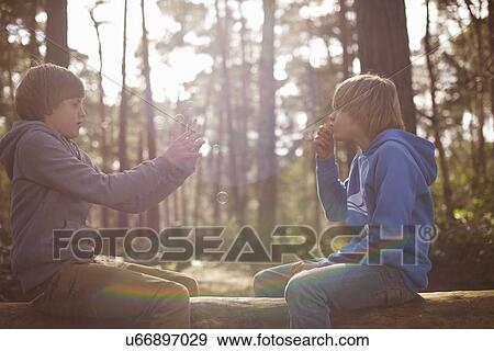 Stock Photo - Twin brothers taking photographs on smartphone in forest. Fotosearch