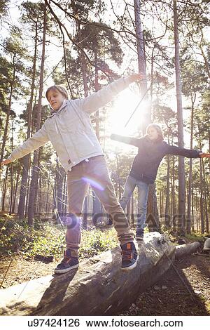 Stock Photograph - Twin brothers walking along fallen tree trunk in forest. Fotosearch
