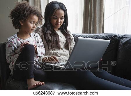Two sisters sitting on sofa using laptop View Large Photo Image Stock Photo - Two sisters sitting on sofa using laptop. Fotosearch