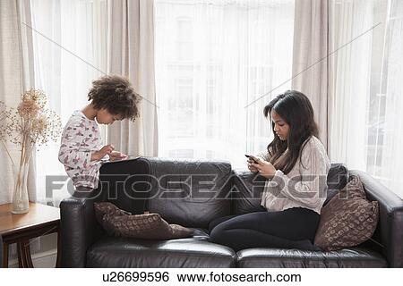 Two sisters sitting on sofa using digital tablet and cellphone View Large Photo Image Stock Photograph - Two sisters sitting on sofa using digital tablet and cellphone. Fotosearch