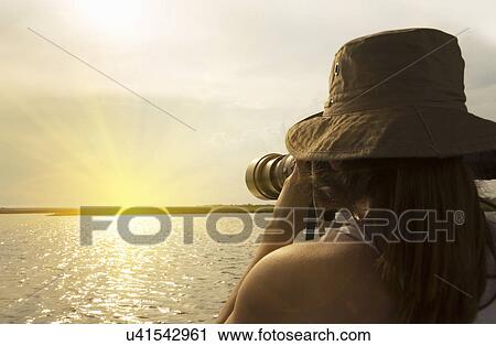 Stock Image - Woman photographing sunset, Kasane, Chobe National Park, Botswana, Africa. Fotosearch