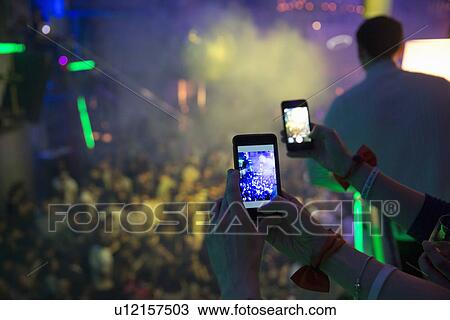 Stock Image - Women taking photograph in nightclub with cellular phone. Fotosearch