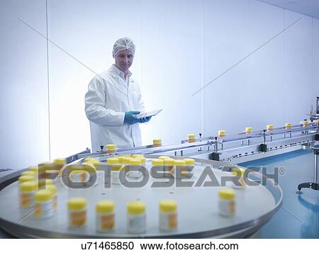 Stock Image - Worker inspecting packaging in pharmaceutical factory. Fotosearch