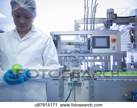 Stock Image - Worker inspecting products on production line in pharmaceutical factory. Fotosearch