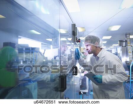 Stock Image - Worker inspecting tablets as they are put into packaging in pharmaceutical factory. Fotosearch