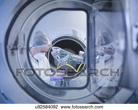 Stock Image - Worker inspects tablets in coating machine in pharmaceutical factory. Fotosearch