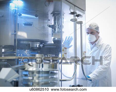 Stock Image - Worker with tablet pressing machine in pharmaceutical factory. Fotosearch